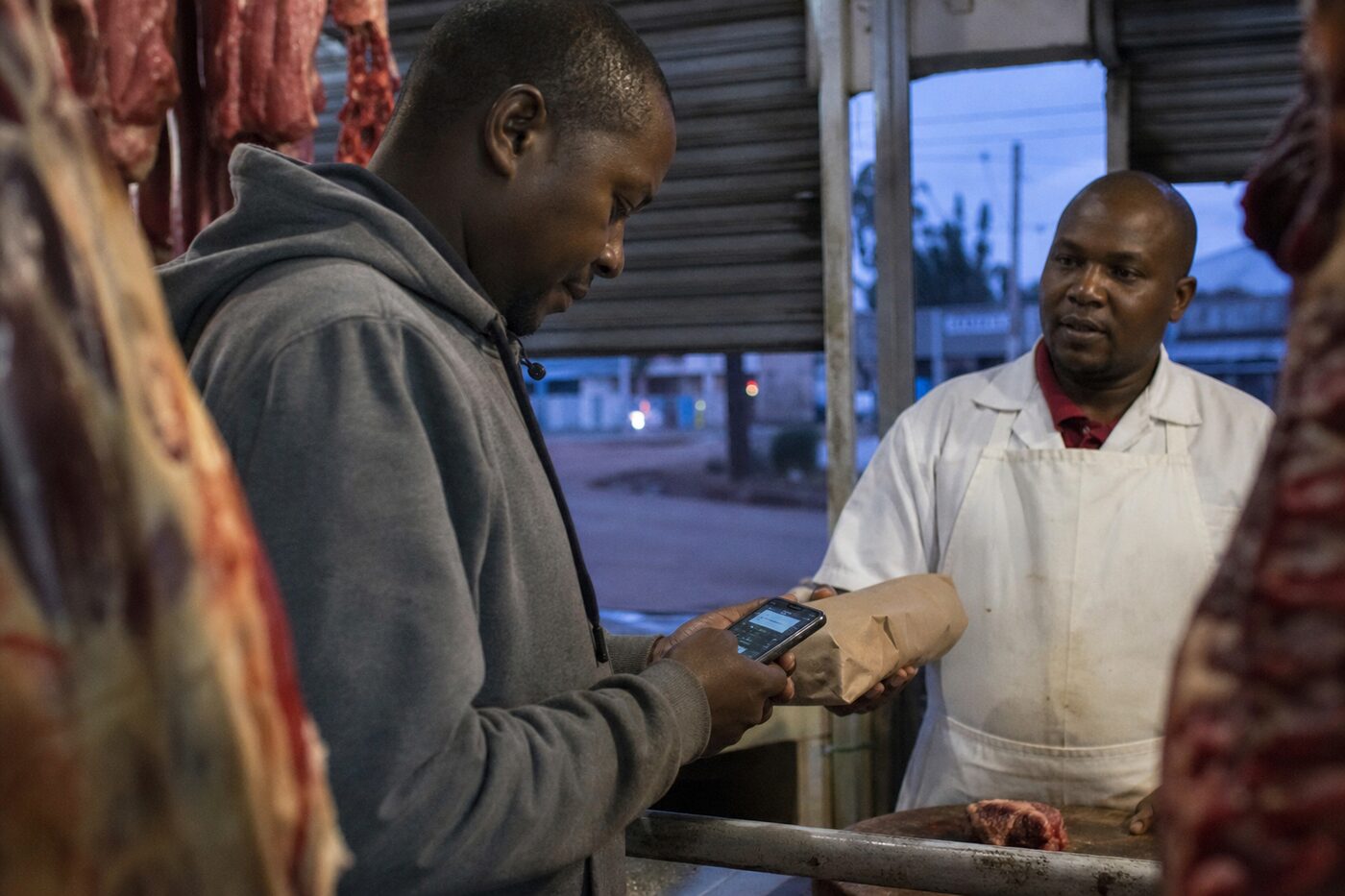 Customer at a butcher counter looking at a phone while waiting for a parcel
