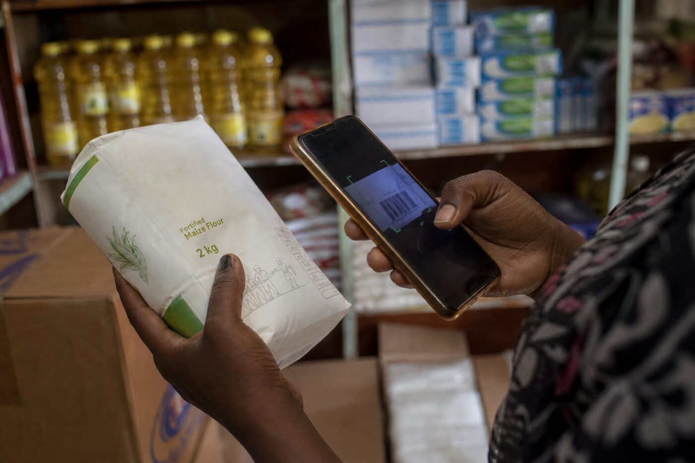 Hands scanning a maize flour barcode with a phone camera in a grocery